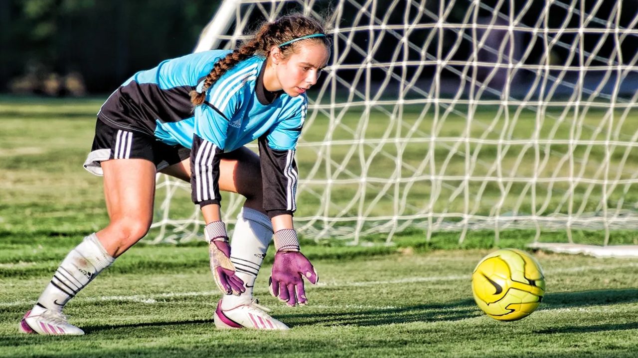 Female soccer goalie diving for ball.