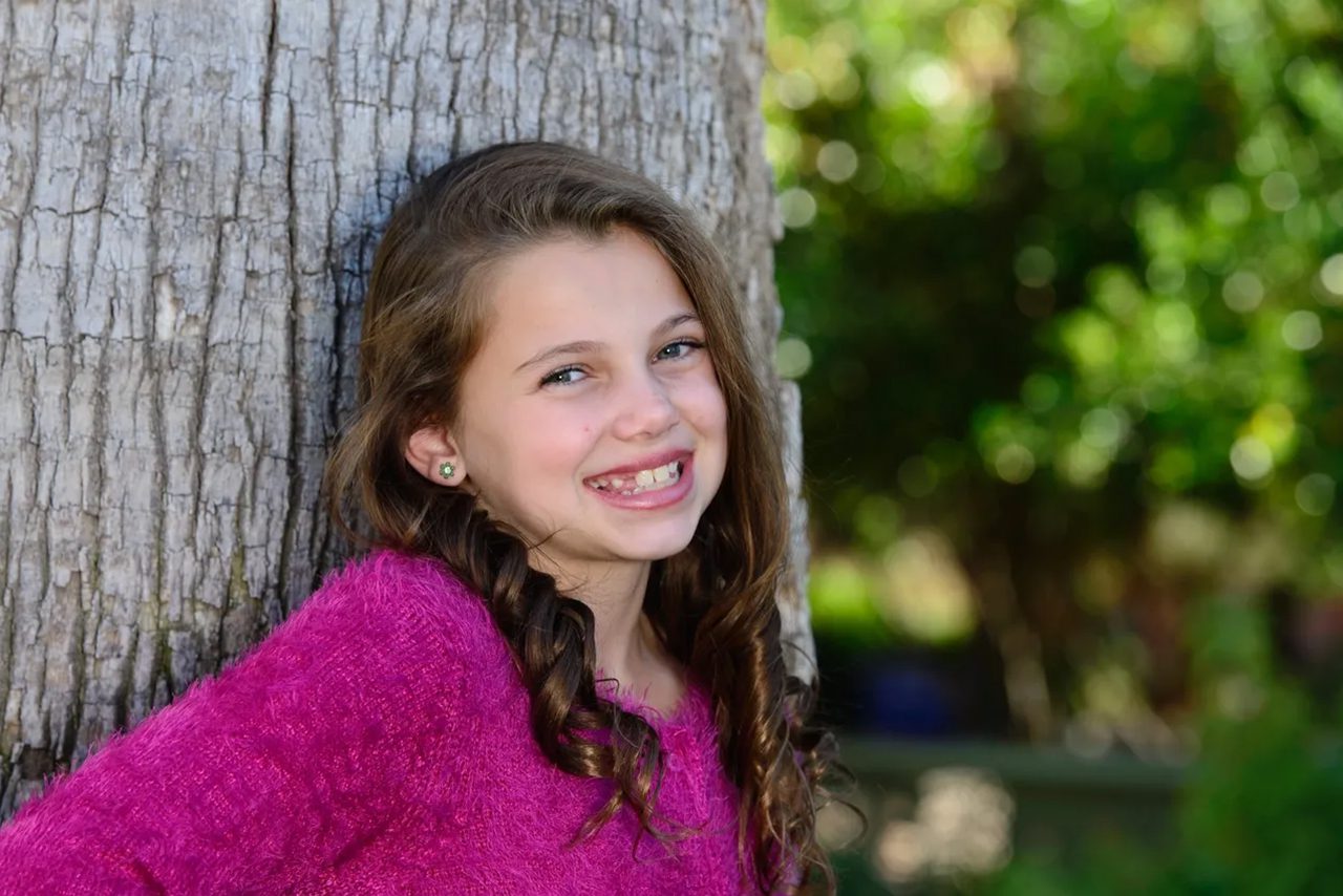 Smiling girl in pink sweater outdoors.