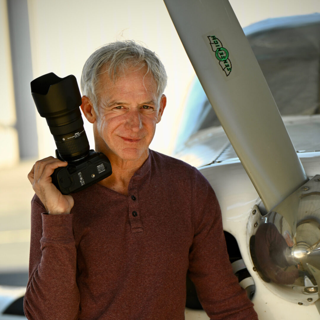 A man holding a camera in front of an airplane.